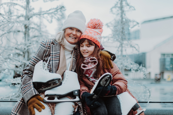 Grandmother with granddaughter in a winter at outdoor ice skating rink. Grandparents teaching cute girl how to ice skating.