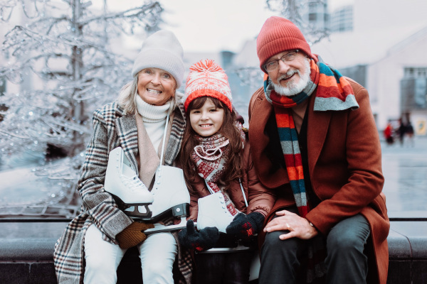 Portrait of seniors and their granddaughter in a winter at outdoor ice skating rink.