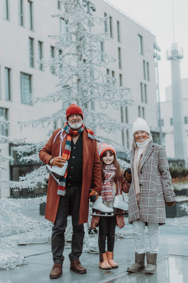 Grandparents with granddaughter at outdoor ice skating rink during cold winter day. Grandparents teaching cute girl how to ice skating.