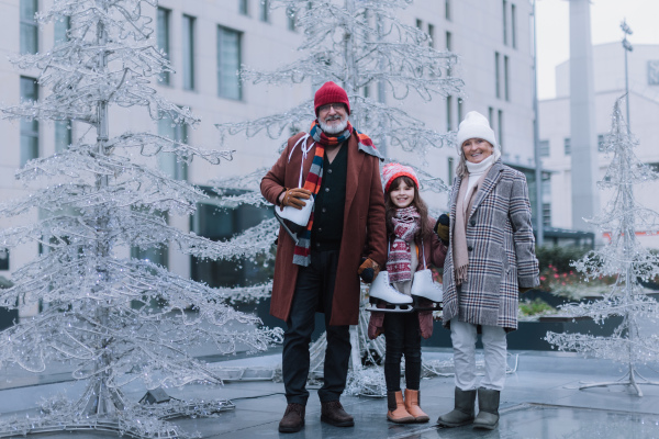 Seniors with their granddaughter in a winter at outdoor ice skating rink. Grandparents teaching cute girl how to ice skating.