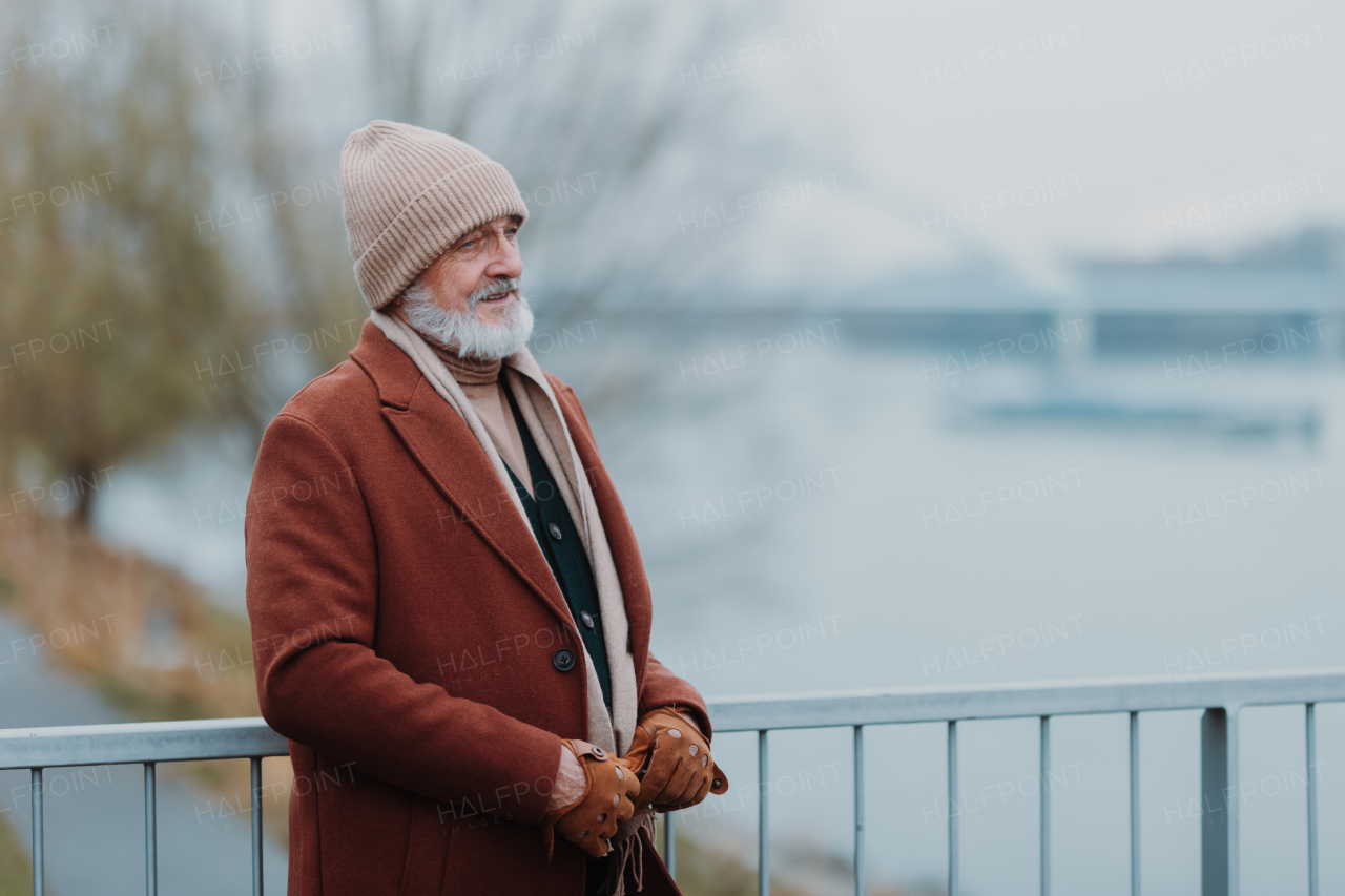 Elegant senior man walking near a river, during cold winter day. Winter shot with copy space.