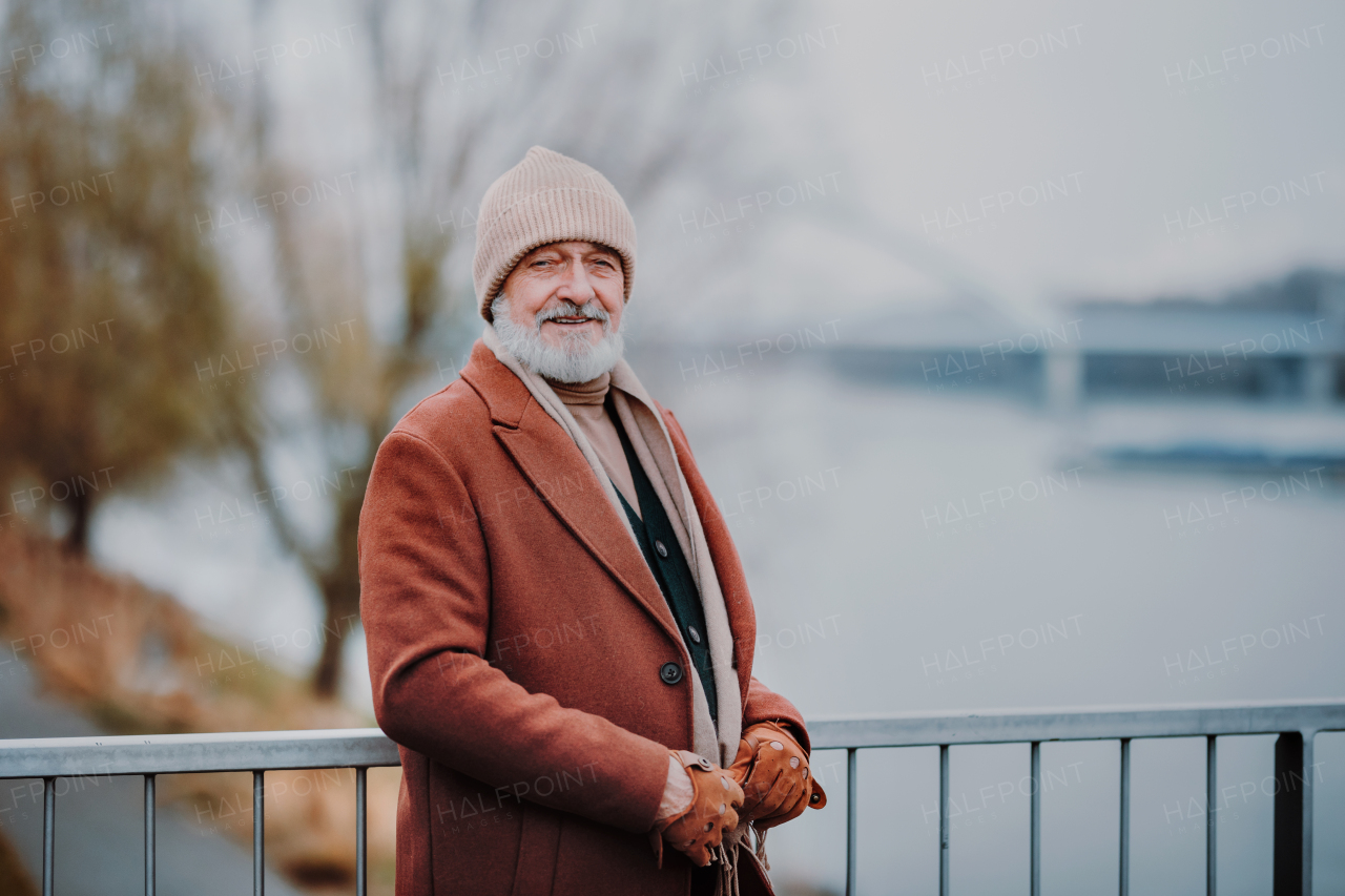 Elegant senior standing near a river, during cold winter day.