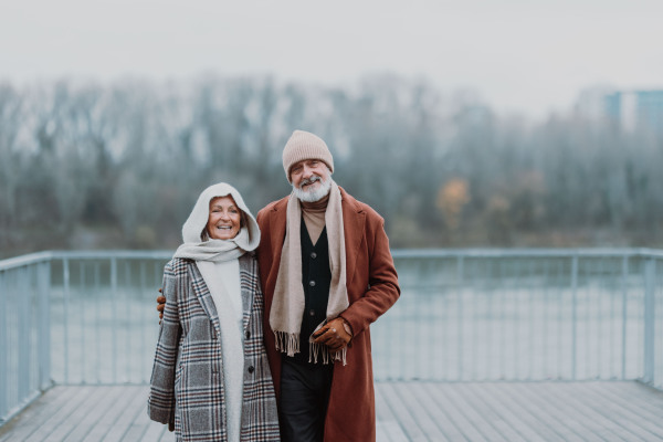 Elegant senior couple walking near a river, during cold winter day.