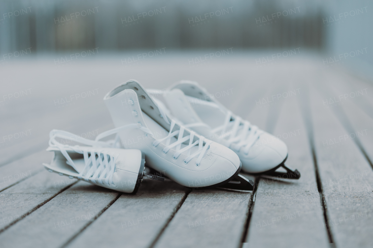 Two pairs of white ice skates placed on wooden floor. Children's and adult women's skates for daughter and mother. Learning to skate together.