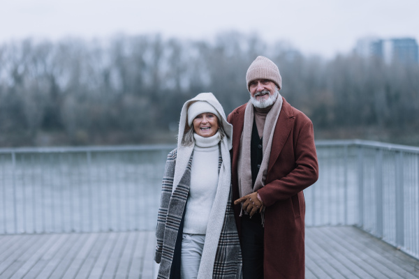 Elegant senior couple walking near a river, during cold winter day.