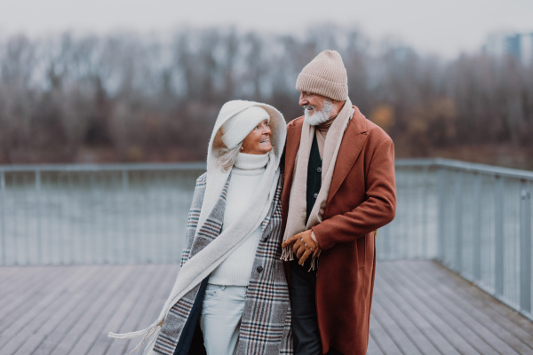 Elegant senior couple walking near a river, during cold winter day.