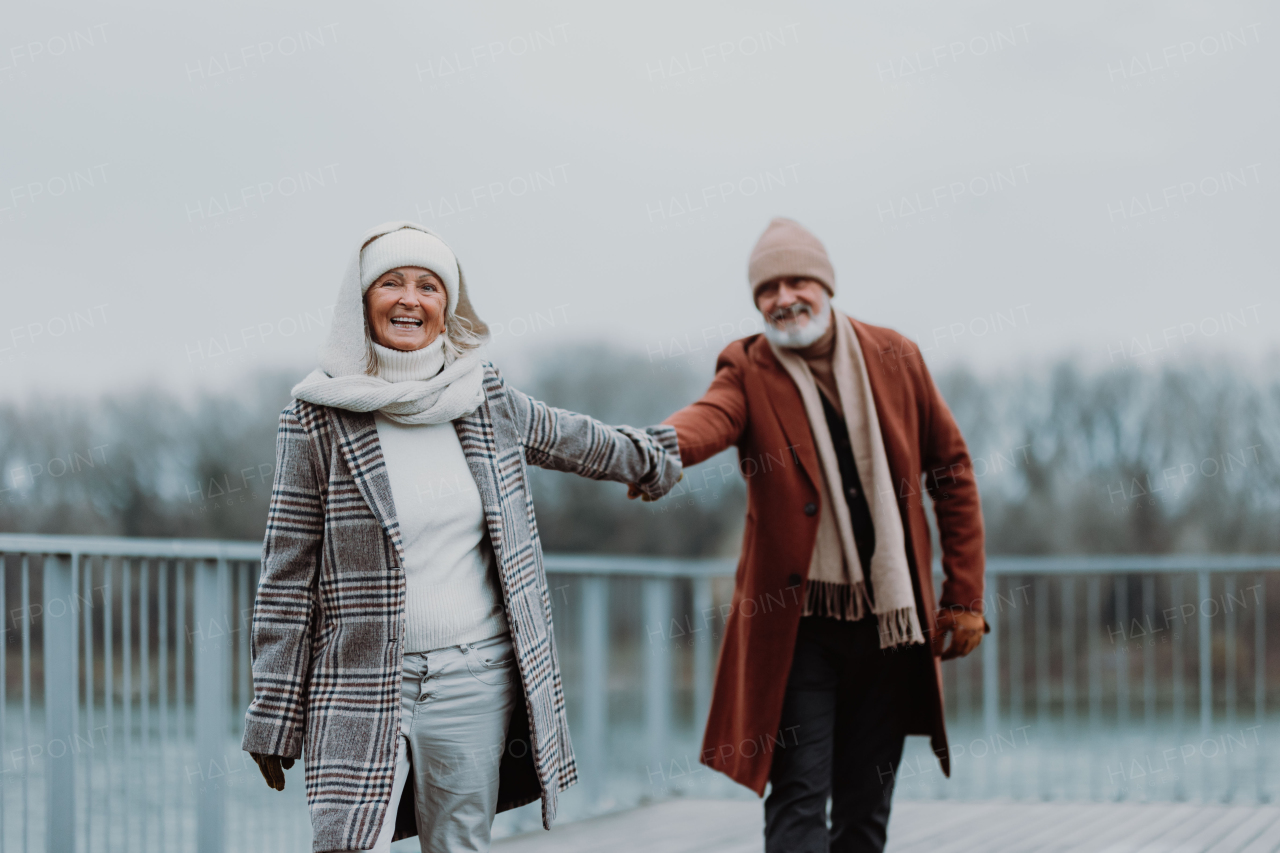 Elegant senior couple walking near a river, during cold winter day.