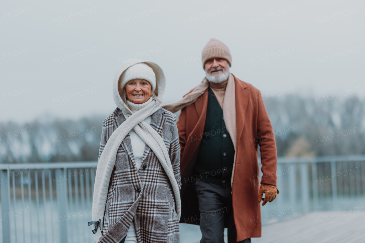 Elegant senior couple walking near a river, during cold winter day.