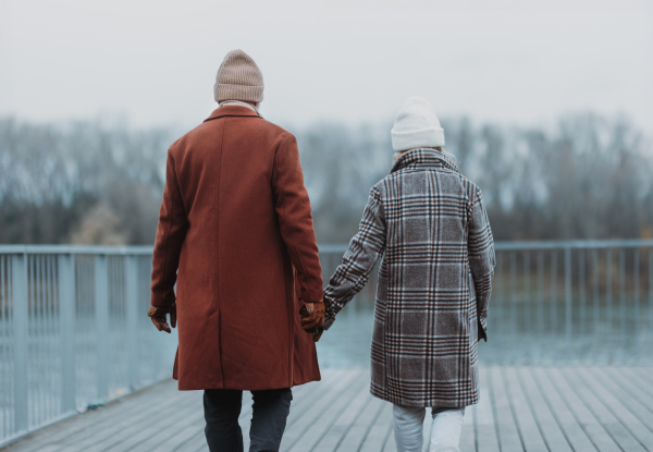 Rear view of elegant senior couple walking near a river, during cold winter day.