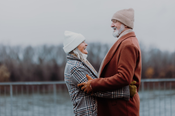 Elegant senior couple walking near a river, during cold winter day.