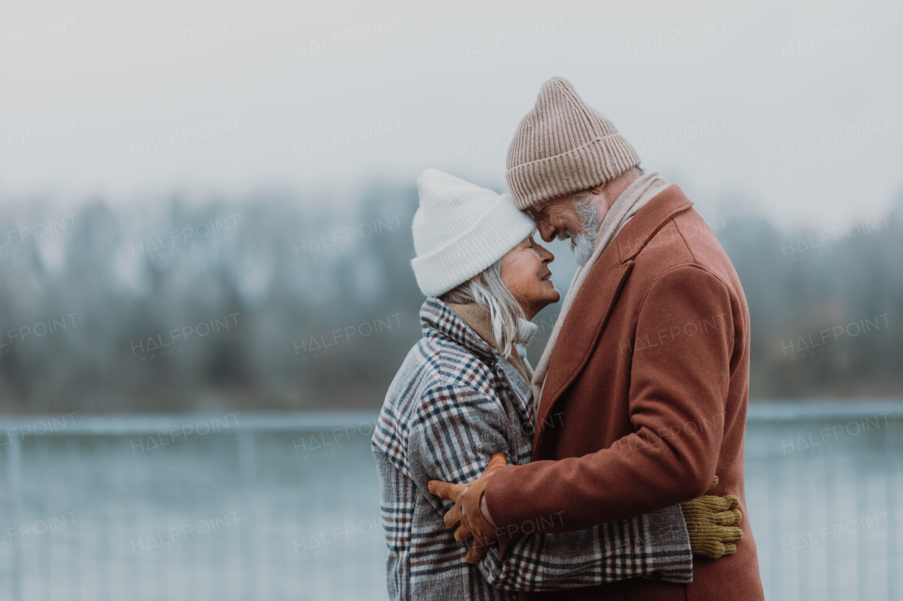 Elegant senior couple embracing near a river, during cold winter day. Love and romantic relationship in retirement.