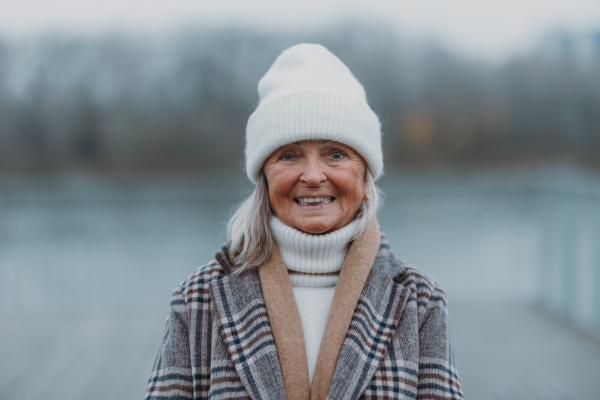 Elegant senior woman walking near a river, during cold winter day. Winter banner with copy space.