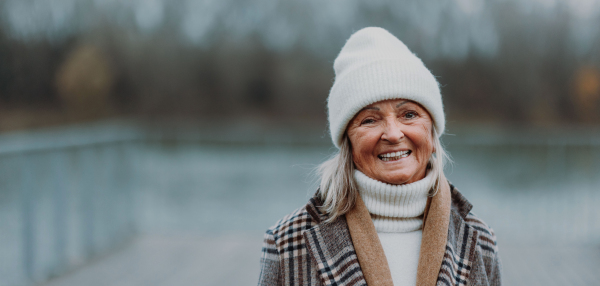 Elegant senior woman walking near a river, during cold winter day. Winter banner with copy space.