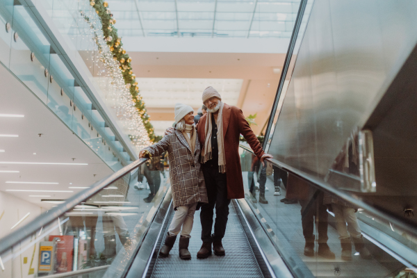 Senior couple on an escalator in a shopping mall, Christmas shopping in the city. Elderly man and woman preparing for Christmas eve.