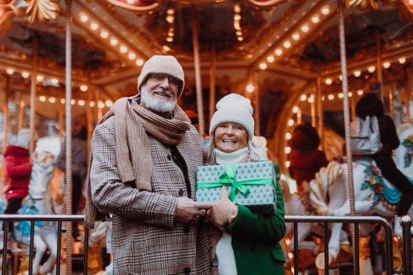 Happy senior couple enjoying outdoor christmas market, buying gifts.