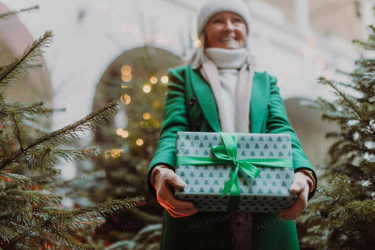 Senior woman standing outdoors, holding a lot of Chrismtas gifts in her hands. Christmas shopping spree.