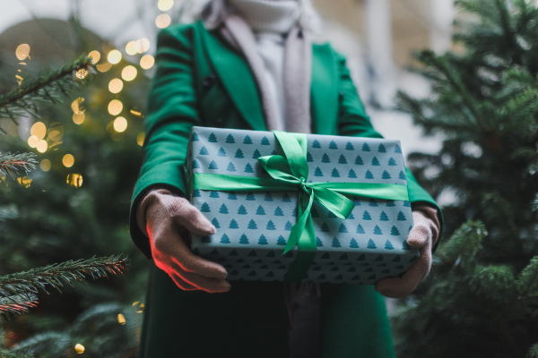 Close up of woman holding christmas gift at christmas market. Buying gifts and christmas tree at outdoor christmas market,