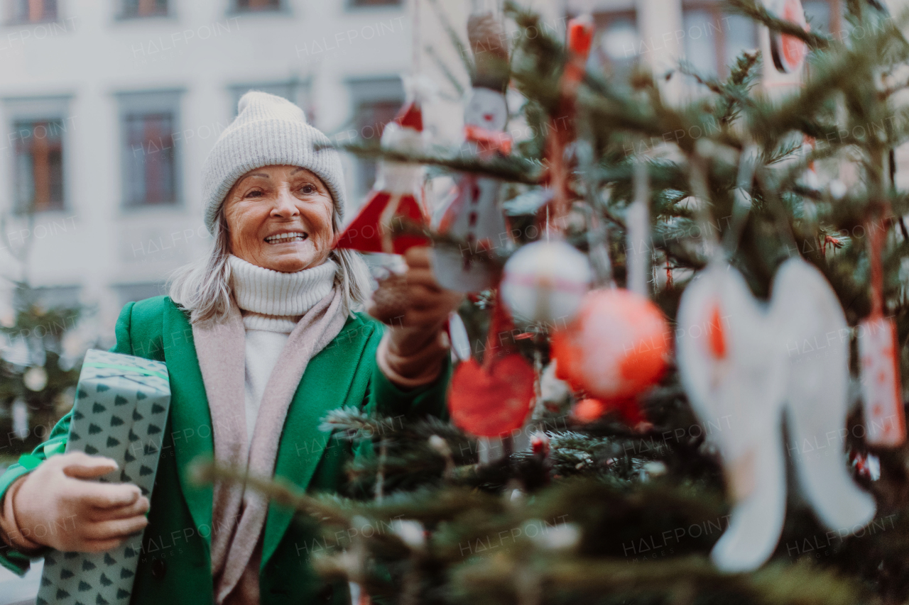 Happy senior woman enjoying outdoor christmas market, buying gifts and Christmas ornaments.