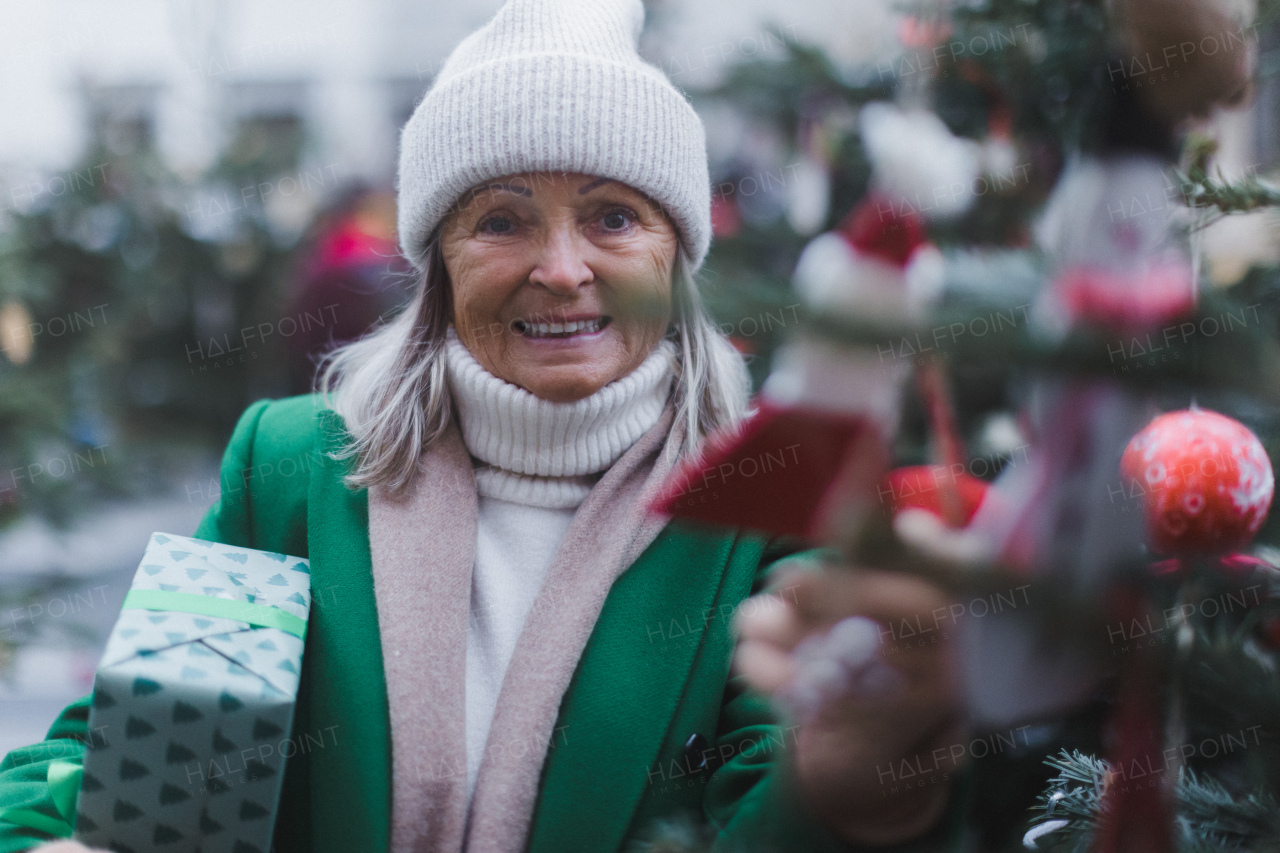 Happy senior woman enjoying outdoor christmas market, buying gifts and Christmas ornaments.