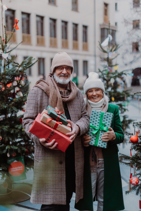 Happy senior couple enjoying outdoor christmas market at the evening, buying gifts and christmas tree.