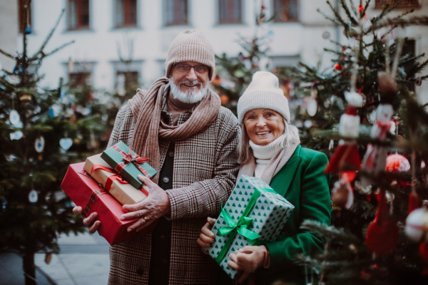 Happy senior couple enjoying outdoor christmas market, buying gifts and christmas tree.