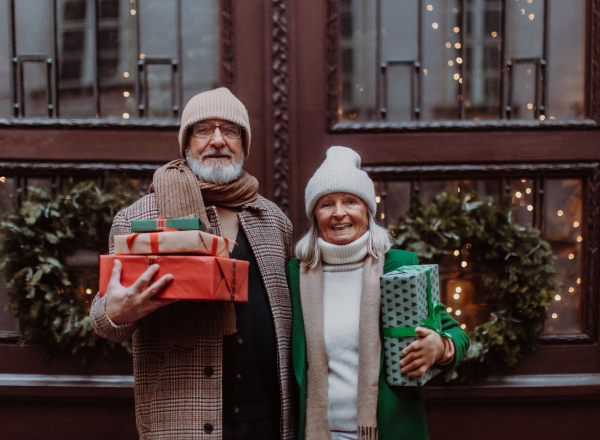 Happy senior couple enjoying outdoor christmas market at the evening, buying gifts and christmas tree.