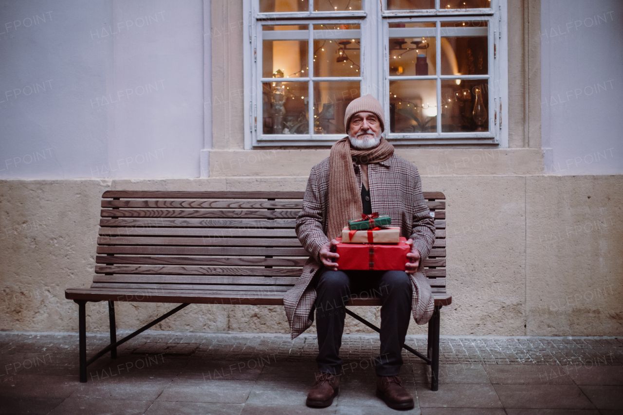 Senior man sitting alone on a bench, holding Chrismtas gifts.