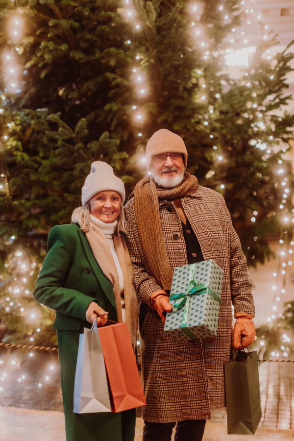 Happy senior couple enjoying outdoor christmas market at the evening, buying gifts and christmas tree.