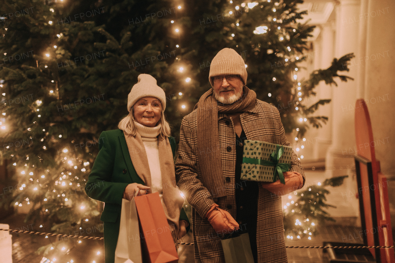 Happy senior couple enjoying outdoor christmas market at the evening, buying gifts and christmas tree.