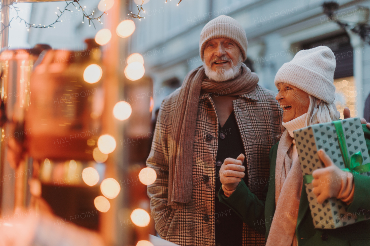 Happy senior couple enjoying outdoor christmas market at the evening, buying gifts.