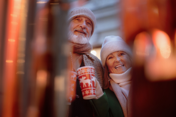 Happy senior couple enjoying outdoor christmas market, drinking punch.