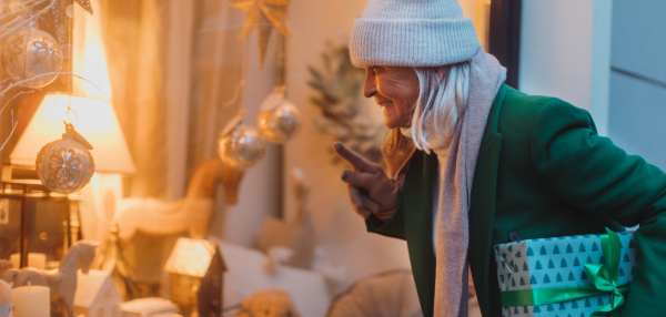 Elegant elderly woman is looking at a window display. The senior lady is shopping for Christmas gifts in the city. Banner with copy space.