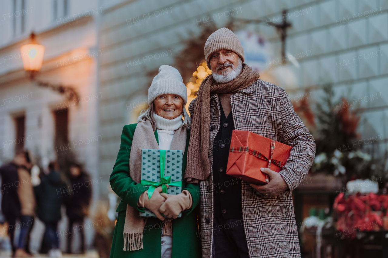 Happy senior couple enjoying outdoor christmas market at the evening, buying gifts and christmas tree.