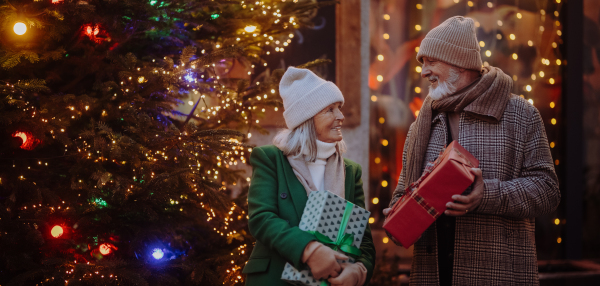 Happy senior couple enjoying outdoor christmas market, buying gifts.