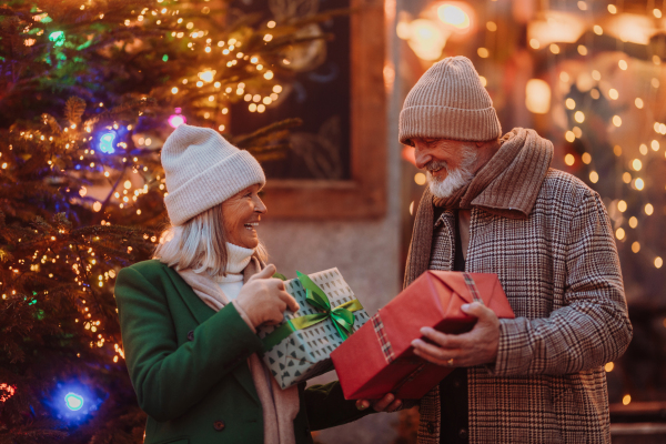 Happy senior couple enjoying outdoor christmas market at the evening, buying gifts and christmas tree.