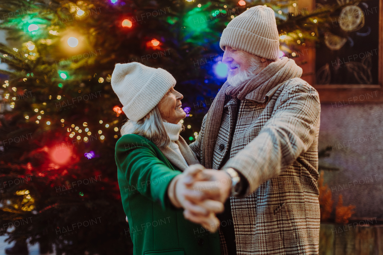 Senior couple having romantic time at outdoor christmas market, dancing near a christmas tree.