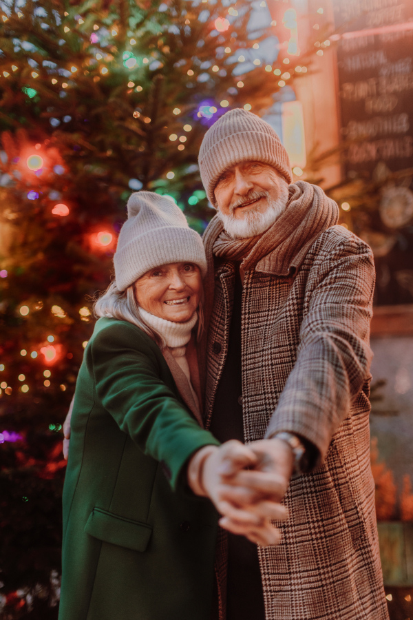 Happy senior couple enjoying outdoor christmas market at the evening, having fun, meeting friends.