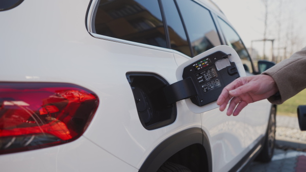 Close up of a senior man charging electric car.