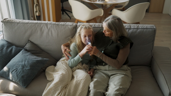 LIttle sick girl using an inhaler during flu with help of her grandmother.