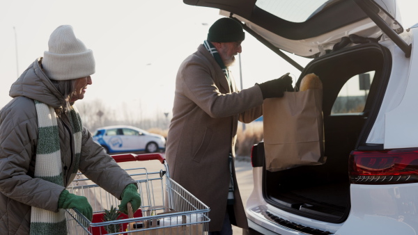 Senior couple giving their purchase in the electric car trunk.