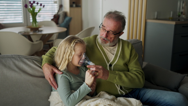 LIttle sick girl using an inhaler during flu with help of her grandfather.