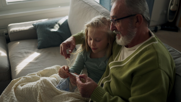 Senior man taking care of his sick granddaughter, measuring her temperature.