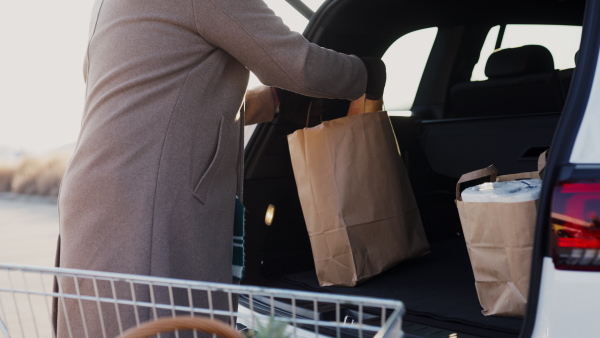 Close up of senior man giving his purchase in the electric car trunk.