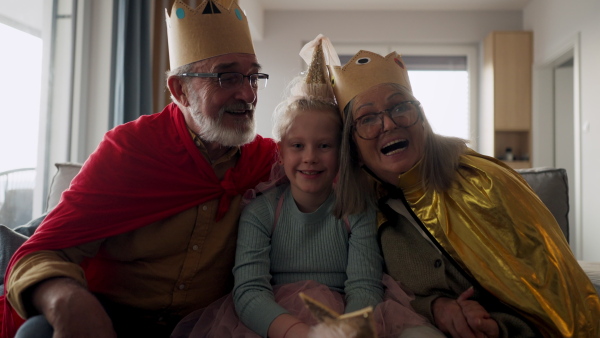 Grandparents playing with their little granddaughter, having costumes of king and queen.