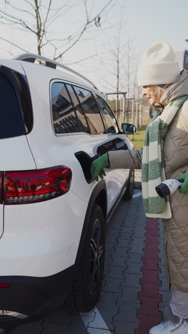 Vertical view of a senior woman charging electric car.