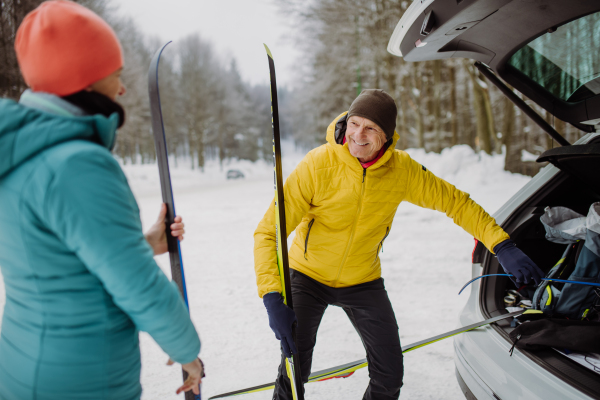 Senior couple near a car trunk preparing for winter skiing.