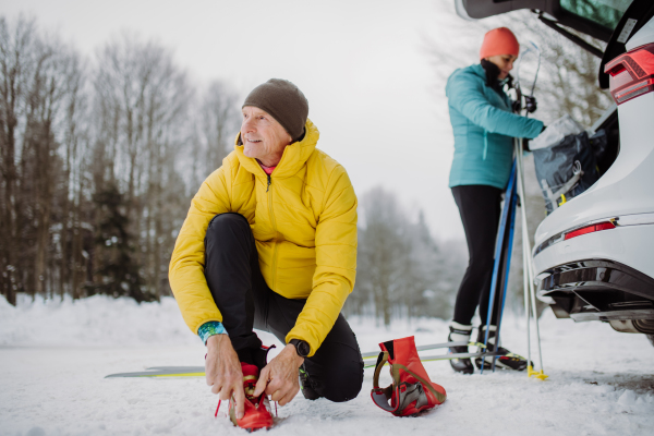 Senior couple near a car trunk preparing for winter skiing.