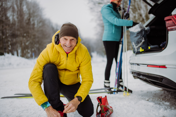 Senior couple near a car trunk preparing for winter skiing.