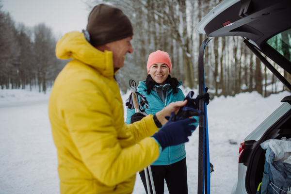 Senior couple near a car trunk preparing for winter skiing.