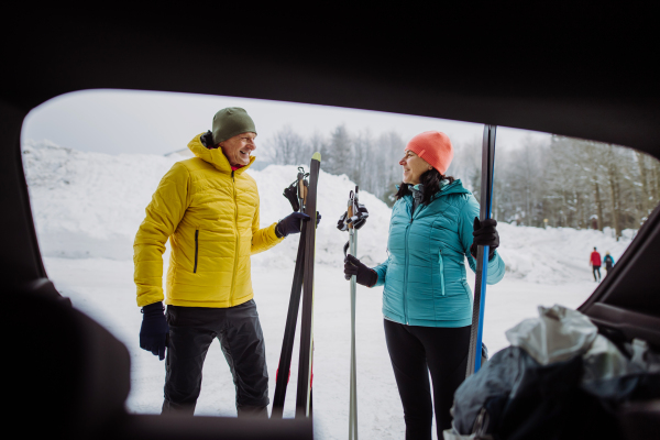 Senior couple near a car trunk preparing for winter skiing.